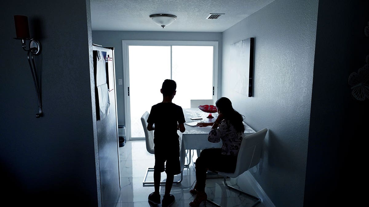 The mother of two, right, sits with her son in the kitchen of their home Tuesday, April 19, 2022, in Tampa, Fla. More immigrants from Cuba are coming to the U.S. by making their way to Mexico and crossing the border illegally. It’s a very different reality from years ago, when Cubans enjoyed special protections that other immigrants did not have. (AP Photo/Chris O'Meara)