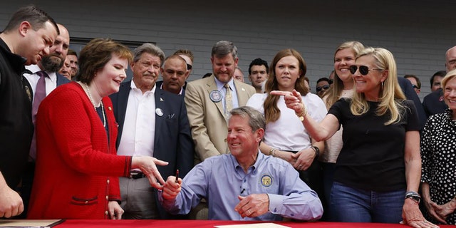Gov. Brian Kemp hands a pen to Rep. Mandi Ballinger after he signed a bill which will allow permit less carry at a sporting goods store in Douglasville, Ga., Tuesday, April 12, 2022. (Bob Andres/Atlanta Journal-Constitution via AP)