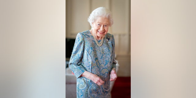 Queen Elizabeth II, who wore a blue patterned dress and a three-strand pearl necklace, was all smiles as she shook hands with guests and posed for photos at Windsor Castle on April 28, 2022.