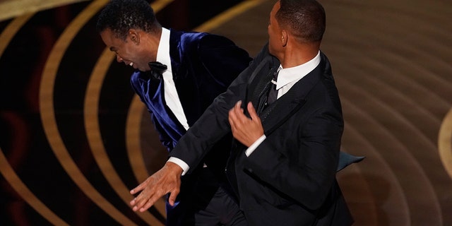 Will Smith hits presenter Chris Rock on stage while Rock presents the award for best documentary feature at the Oscars.