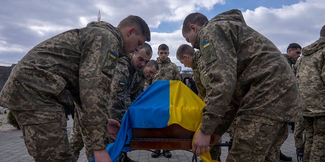 Des soldats placent le drapeau ukrainien sur le cercueil du soldat Simakov Oleksandr, 41 ans, lors de sa cérémonie funéraire, après qu'il a été tué au combat, au cimetière Lychakiv, à Lviv, dans l'ouest de l'Ukraine, le lundi 4 avril 2022. 