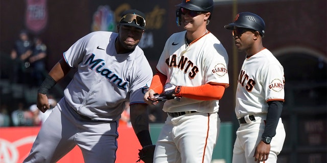 Miami Marlins first baseman Jesus Aguilar, left, congratulates San Francisco Giants' Joc Pederson, middle, after his base hit during the ninth inning of a game in San Francisco April 9, 2022. At right is Giants first base coach Antoan Richardson.