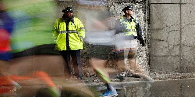 Police officers stand watch as Boston Marathon runners race along the course, April 20, 2015, in Boston.