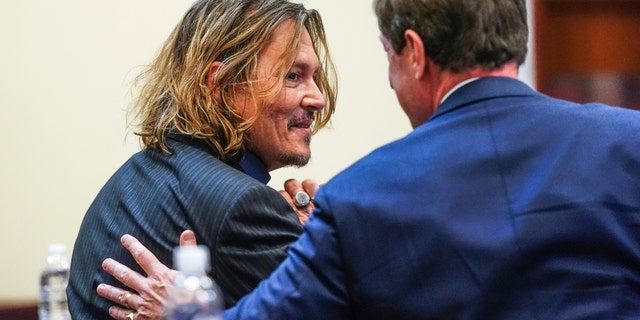 Johnny Depp smiles while sitting with his legal team on April 14, 2022, at the Fairfax County Circuit Court in Fairfax, Virginia. 