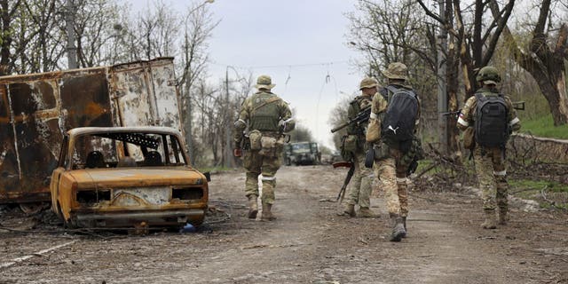 Servicemen of Donetsk People's Republic militia walk past damaged vehicles during a heavy fighting in an area controlled by Russian-backed separatist forces in Mariupol, Ukraine, Tuesday, April 19, 2022. Taking Mariupol would deprive Ukraine of a vital port and complete a land bridge between Russia and the Crimean Peninsula, seized from Ukraine from 2014. 