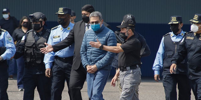 Former Honduran President Juan Orlando Hernandez, center, is taken in handcuffs to a waiting aircraft as he is extradited to the United States, at an Air Force base in Tegucigalpa, Honduras, Thursday, April 21, 2022. 