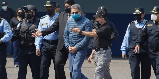 Former Honduran President Juan Orlando Hernandez, center, is taken in handcuffs to a waiting aircraft as he is extradited to the United States, at an Air Force base in Tegucigalpa, Honduras, Thursday, April 21, 2022.