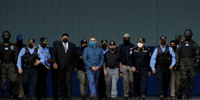 Former Honduran President Juan Orlando Hernandez, center, wearing a blue protective face mask and handcuffed, is escorted under heavy guard to a waiting aircraft at the Air Force base in Tegucigalpa, Honduras, Thursday, April 21, 2022. 
