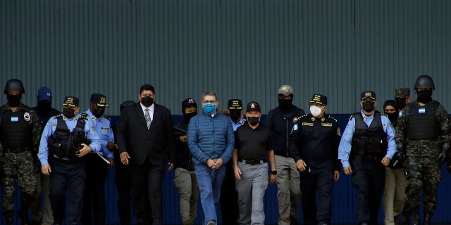 Former Honduran President Juan Orlando Hernandez, center, wearing a blue protective face mask and handcuffed, is escorted under heavy guard to a waiting aircraft at the Air Force base in Tegucigalpa, Honduras, Thursday, April 21, 2022. 