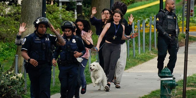 Police evacuate people, including Sarah Cope running with her dog, near the scene of a shooting Friday, April 22, 2022, in northwest Washington. At least four people were shot when a gunman unleashed a flurry of bullets in the nation’s capital. The hail of gunfire led to lockdowns at several schools and left a community on edge before the suspect was found dead hours later.  