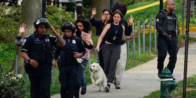 Police evacuate people, including Sarah Cope running with her dog, near the scene of a shooting Friday, April 22, 2022, in northwest Washington. At least four people were shot when a gunman unleashed a flurry of bullets in the nation’s capital. The hail of gunfire led to lockdowns at several schools and left a community on edge before the suspect was found dead hours later.