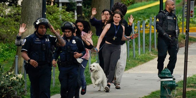 Police evacuate people, including Sarah Cope running with her dog, near the scene of a shooting Friday, April 22, 2022, in northwest Washington. At least four people were shot when a gunman unleashed a flurry of bullets in the nation’s capital. The hail of gunfire led to lockdowns at several schools and left a community on edge before the suspect was found dead hours later.  