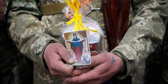 A Ukrainian soldier holds an Easter cake and an icon during a blessing ceremony on Easter eve at a military position outside Kyiv, Ukraine, Saturday, April 23, 2022. (AP Photo/Efrem Lukatsky)