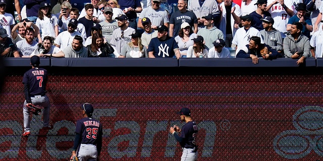 The Cleveland Guardians' Myles Straw (7) climbs the left field wall to talk with a fan during the ninth inning of a game against the New York Yankees Saturday, April 23, 2022, in New York. The Yankees won 5-4. 