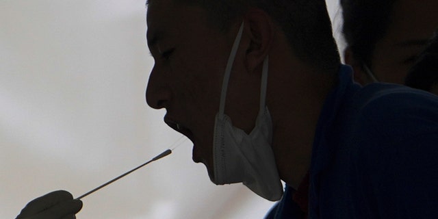 A worker has a throat swab sample taken at a coronavirus test site set up near a commercial office complex, Sunday, April 24, 2022, in Beijing. Beijing is on alert after 10 middle school students tested positive for COVID-19, in what city officials said was an initial round of testing.