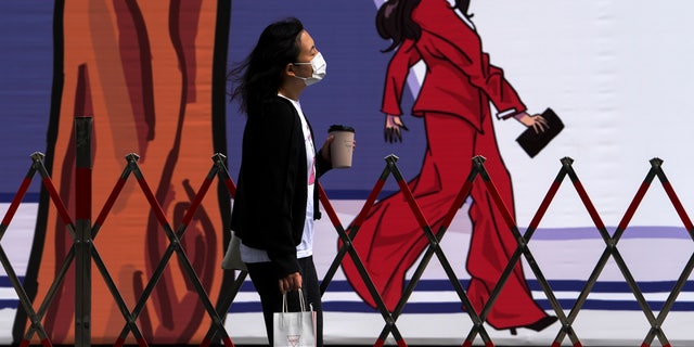 A woman wearing a face mask to help protect from the coronavirus walks by a barricaded construction wall displaying a fashion cartoon at a mall Sunday, April 24, 2022, in Beijing. Beijing is on alert after 10 middle school students tested positive for COVID-19, in what city officials said was an initial round of testing.