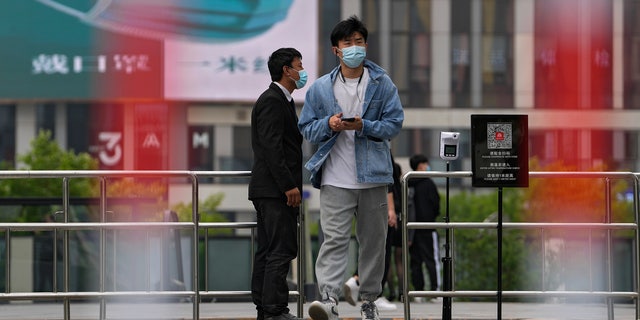 A man wearing a face mask walks by a masked security stands guard at a barricaded entrance displaying a health QR code and a temperature scanner at a commercial office complex, Sunday, April 24, 2022, in Beijing. Beijing is on alert after 10 middle school students tested positive for COVID-19, in what city officials said was an initial round of testing. 