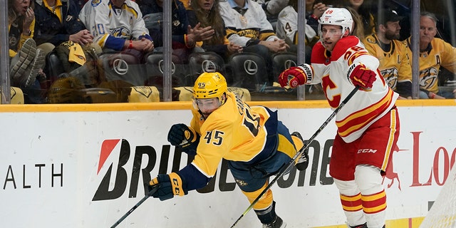 Nashville Predators' Alexandre Carrier (45) falls as he chases the puck with Calgary Flames' Elias Lindholm (28) in the first period of an NHL hockey game Tuesday, April 26, 2022, in Nashville, Tenn. 