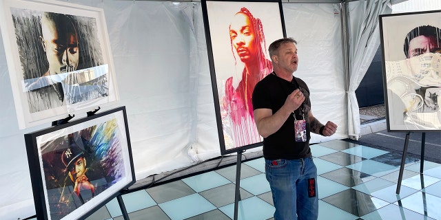 In a photo provided by Marc Ganis, artist Rob Prior stands in front of several previous works, including one of Snoop Dogg from the Super Bowl halftime show in February, on Wednesday, April 27, 2022, in Las Vegas. Prior will be painting portraits of each NFL football draftee through the first round Thursday night.