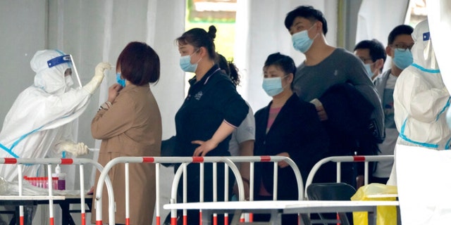 A worker in a protective takes a swab for a COVID-19 test at a coronavirus testing facility in Beijing, Saturday, April 23, 2022. Beijing is on alert after 10 middle school students tested positive for COVID-19 on Friday, in what city officials said was an initial round of testing. 