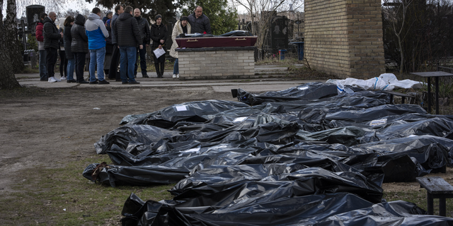 A family mourns a relative killed during the war with Russia, as dozens of black bags containing more bodies of victims are seen strewn across the graveyard in the cemetery in Bucha, in the outskirts of Kyiv, Ukraine, on Monday.