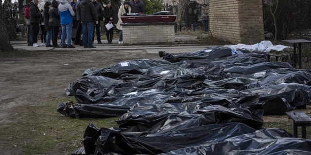 A family mourns a relative killed during the war with Russia, as dozens of black bags containing more bodies of victims are seen strewn across the graveyard in the cemetery in Bucha, in the outskirts of Kyiv, Ukraine, on Monday.