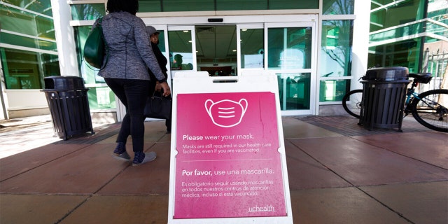 A sign advising visitors to don face coverings stands outside the main entrance to UCHealth University of Colorado hospital Friday, April 1, 2022, in Aurora, Colo.
