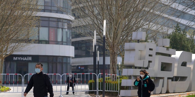 Residents wearing face masks walk by a masked security watch over a barricaded Galaxy Soho commercial office building which was locked down for health monitoring following a COVID-19 case detected in the area, Tuesday, April 5, 2022, in Beijing.