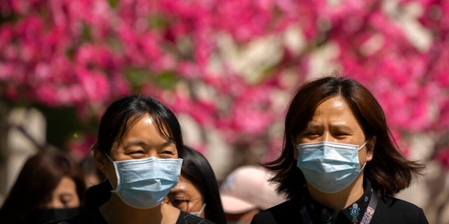 People wearing face masks walk near blossoming trees at a public park in Beijing, Thursday, April 14, 2022.
