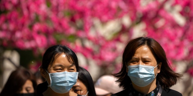 People wearing face masks walk near blossoming trees at a public park in Beijing, Thursday, April 14, 2022.