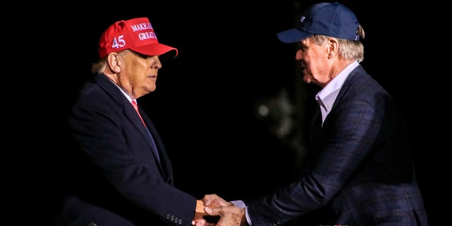 Donald Trump shakes hands with former Sen. David Perdue, who's primary challenging GOP Gov. Brian Kemp, at the former president's rally in Cumming, Georgia, on March 26, 2022.