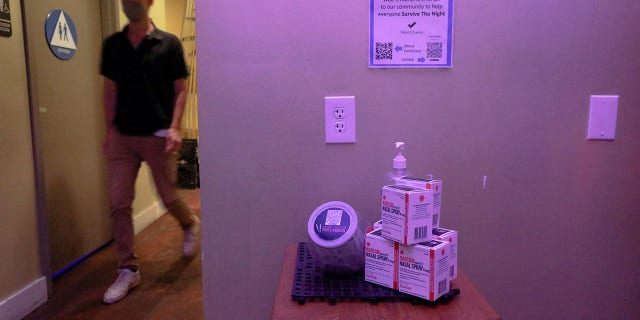 A patron walks near a table with free fentanyl test strips and Narcan at Low Bar in Oakland, California, on March 3, 2022.
