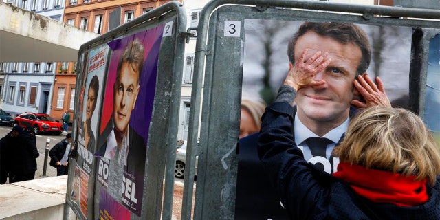 A woman touches the presidential campaign poster of French President Emmanuel Macron during the first round of the French presidential election, in Strasbourg, eastern France, Sunday April 10, 2022.