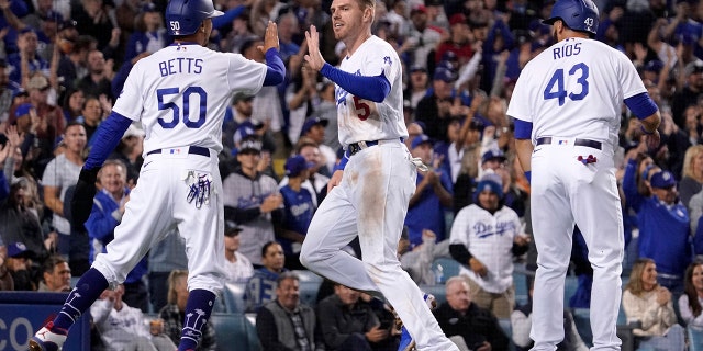 Los Angeles Dodgers' Freddie Freeman, center, is congratulated by Mookie Betts, left, and Edwin Rios after they scored on a double by Trea Turner during the fourth inning of a baseball game against the Atlanta Braves Monday, April 18, 2022, in Los Angeles.