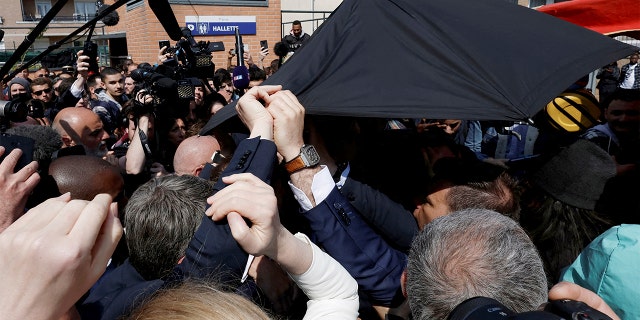 French President Emmanuel Macron is protected with an umbrella after a projectile was thrown during a walk in the Saint-Christophe market square in Cergy, a suburb of Paris, on Wednesday, April 27, 2022.