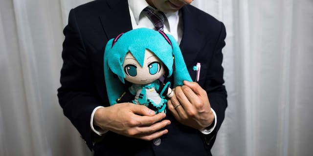 Japanese man Akihiko Kondo poses next to a hologram of Japanese virtual reality singer Hatsune Miku at his apartment in Tokyo, on Nov. 10, 2018, a week after marrying her.