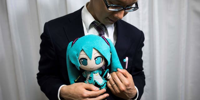 Japanese man Akihiko Kondo poses next to a hologram of Japanese virtual reality singer Hatsune Miku at his apartment in Tokyo, on Nov. 10, 2018, a week after marrying her.
