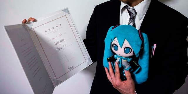 Japanese man Akihiko Kondo poses with a doll of Japanese virtual reality singer Hatsune Miku, as he shows their marriage certificate, at his apartment in Tokyo, on Nov. 10, 2018, a week after marrying her.