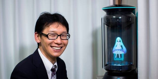 Japanese man Akihiko Kondo poses next to a hologram of Japanese virtual reality singer Hatsune Miku at his apartment in Tokyo, on Nov. 10, 2018, a week after marrying her.