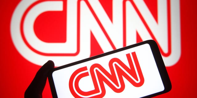 In this photo illustration a CNN (Cable News Network) logo is seen on a smartphone and a PC screen.