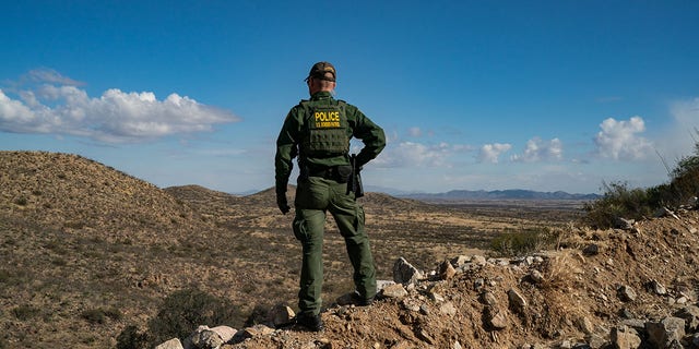 SASABE, ARIZONA - JANUARY 23: A US Border Patrol agent stands on a cliff looking for migrants who crossed the US-Mexico border wall near Sasabe, Arizona on Sunday, January 23, 2022. 