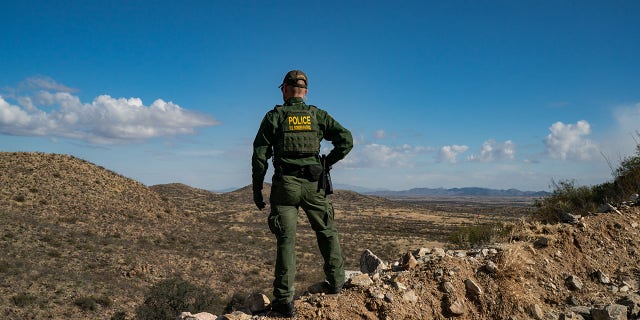 A Border Patrol agent stands on a cliff looking for migrants who crossed into the U.S. from Mexico near the city of Sasabe, Arizona, Jan. 23, 2022.