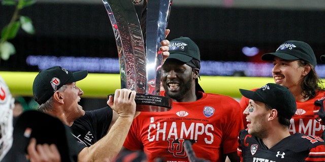 (L-R) Head coach Kyle Whittingham hands the championship trophy to linebacker Devin Lloyd and wide receiver Britain Covey as they celebrate the team's 38-10 victory over the Oregon Ducks to win the Pac-12 Conference championship game at Allegiant Stadium Dec. 3, 2021, in Las Vegas.  