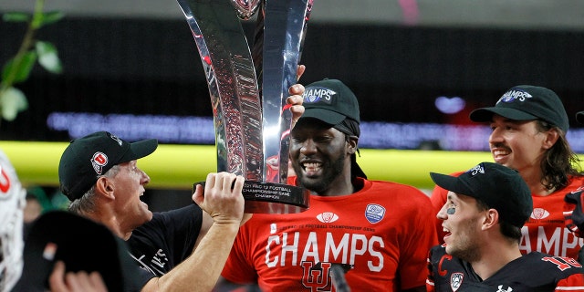 (L-R) Head coach Kyle Whittingham hands the championship trophy to linebacker Devin Lloyd and wide receiver Britain Covey as they celebrate the team's 38-10 victory over the Oregon Ducks to win the Pac-12 Conference championship game at Allegiant Stadium Dec. 3, 2021, in Las Vegas.