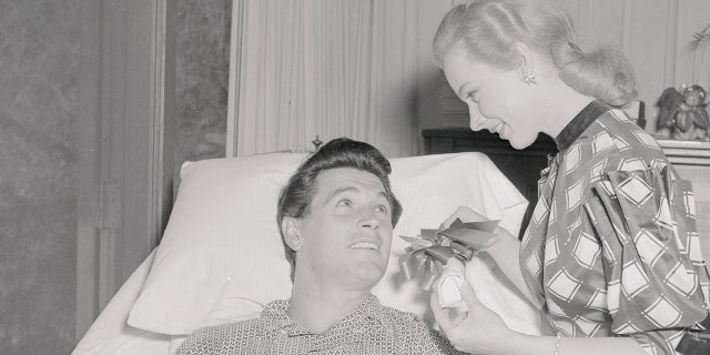 Film star Rock Hudson gets a visit from actress Piper Laurie. The young actor broke his collarbone while surfboarding near Laguna Beach, Calif.
