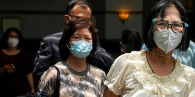 A woman wearing a face mask and shield walks at a commercial building in Hong Kong, Thursday, April 14, 2022.