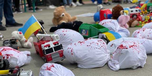 Children's toys are spread out on the ground at an Atlanta park, mixed with fake blood-stained sacks representing children killed in Ukraine.