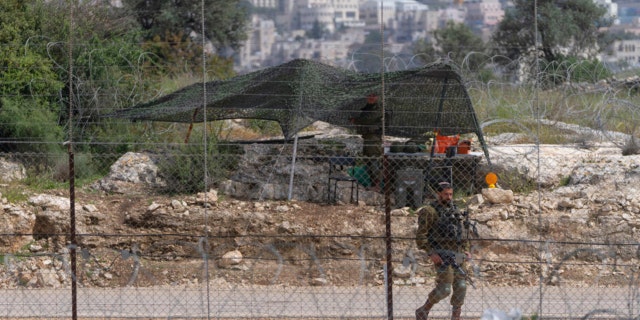 FILE - An Israeli soldier guards an opening in Israel's West Bank separation barrier that was reinforced with barbed wire to prevent Palestinians from crossing into Israel, in the West Bank village of Nilin, west of Ramallah, April 10, 2022. Israeli forces shot and killed a Palestinian man during clashes on Wednesday, April 13, 2022, the Palestinian Health Ministry said, as Israeli troops continued a days-long operation in the occupied West Bank in response to a spate of deadly attacks. The death is the latest in a wave of Israeli-Palestinian violence that has erupted as Muslims mark the holy month of Ramadan.