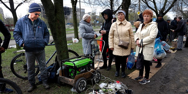 Op vrijdag 22 april 2022 verzamelden de lokale bevolking zich bij een generator om hun mobiele apparaten op te laden in een gebied dat wordt gecontroleerd door door Rusland gesteunde separatistische troepen in Mariupol, Oekraïne.  (AP Foto / Alexei Alexandrov)