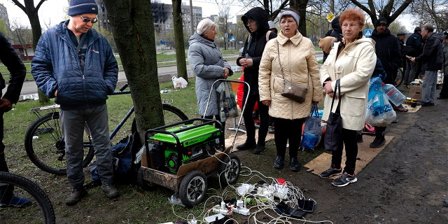 Vietējie iedzīvotāji pulcējas pie ģeneratora, lai uzlādētu savas mobilās ierīces Krievijas atbalstīto separātistu spēku kontrolētajā teritorijā Mariupolē, Ukrainā, piektdien, 2022. gada 22. aprīlī (AP Photo/Aleksejs Aleksandrovs)